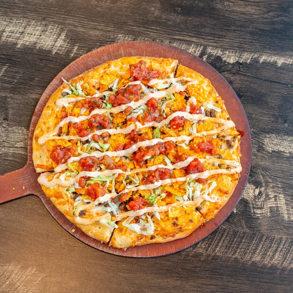 Invictus Pizza Kitchen's taco pizza, topped with salsa, lettuce, and a creamy drizzle, on a wooden paddle.