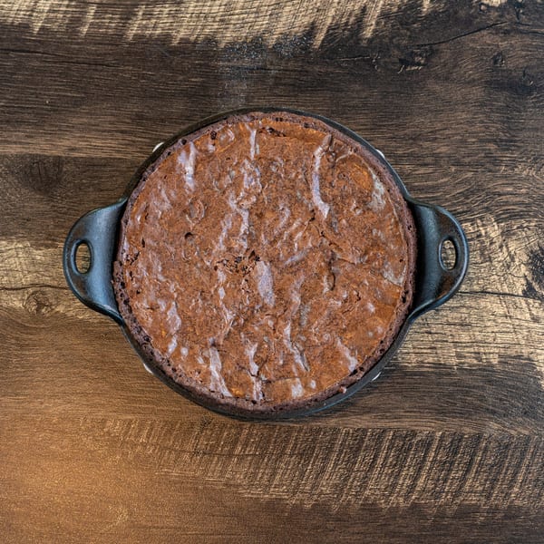 A freshly baked brownie in a black cast iron skillet on a rustic wooden table.